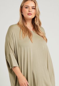 Olivgrön oversized topp med rundad halsringning och korta ärmar. Tillverkad av mjukt, lättviktigt tyg, har en avslappnad passform och en slät yta.