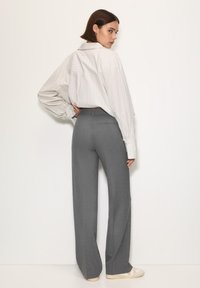 Szare spodnie o prostym kroju, zestawione z luźną białą koszulą w paski. Materiał wydaje się gładki o delikatnej teksturze.