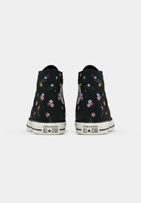 Zwarte canvas sneakers met hoge toppen, voorzien van een bloemenpatroon in verschillende kleuren. Witte rubberen zool met zwarte strepen, Converse-logo op de hiel.