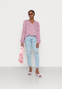 Blusa a stampa floreale in tonalità rosa, vestibilità rilassata, con maniche a sbuffo; jeans strappati blu chiaro; mule con tacco a blocco viola chiaro; borsa rosa.