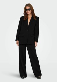Blazer noir surdimensionné avec un seul bouton, poches avant et pantalon large assorti. Tissu lisse avec une coupe ajustée.