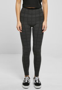 Leggings taille haute noirs et gris avec un motif géométrique texturé, associés à des baskets noires à lacets blancs.