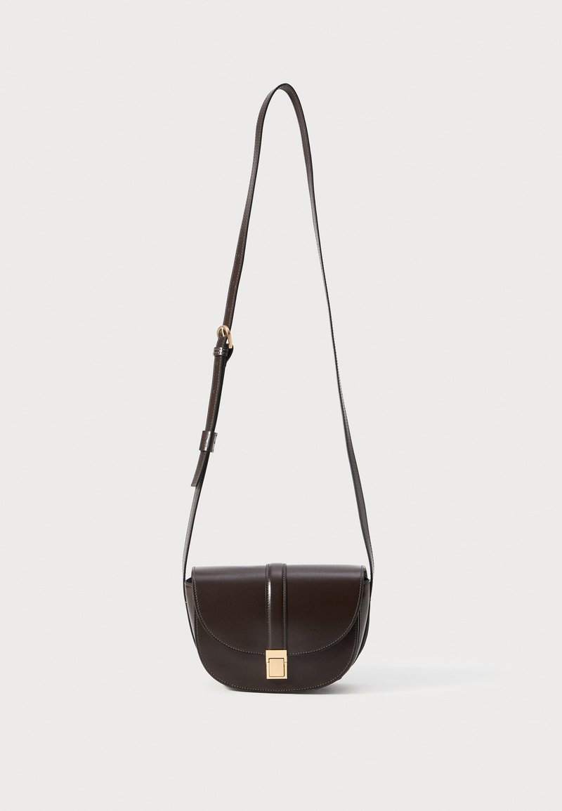 Bolsa de ombro de couro castanho com uma forma curva, apresentando um fecho com aba, detalhes em dourado e uma alça longa ajustável.