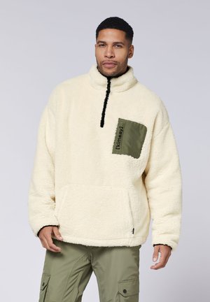 Cremefarbene Fleece-Pullover mit hohem Kragen, schwarzem Reißverschluss und einer olivgrünen aufgenähten Tasche mit Text. Entworfen für Wärme und Komfort.