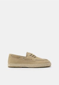 Chaussure beige en daim de style mocassin avec lacets et semelle espadrille tressée, présentée de profil sur un fond blanc.