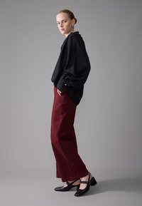 Sort bluse med voluminøse ærmer, parret med bordeaux brede bukser og sorte stiletter med ankelrem. Glat stof og struktureret design.