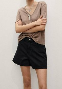 Camiseta marrón de cuello en pico combinada con pantalones cortos de mezclilla negros de tiro alto. El conjunto presenta un ajuste relajado y una textura suave.