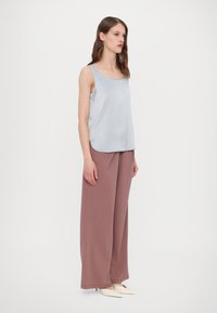 Lichtblauw satijnen tanktop met brede banden, gecombineerd met hooggeknoopte, losse mauve broeken. Glad oppervlak, minimaal design.