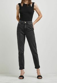 Svart ribbad linne med axelkutt, i kombination med mörkgrå högmidjade jeans, uppvikta vid anklarna, och svarta halkskyddsandaler.