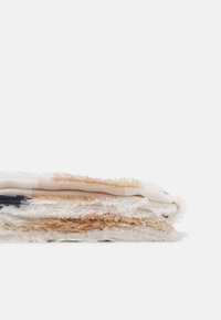 Couverture en coton tissé présentant un design stratifié avec des couleurs crème, beige et marine. Les bords ont une texture effilochée pour plus de détails.