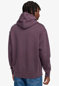 Felpa viola con cappuccio regolabile, polsini e orlo a coste, texture morbida e vestibilità oversize, indossata con jeans di jeans blu.