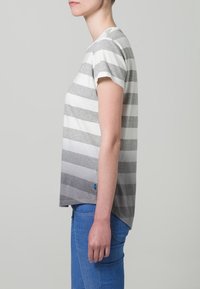 Randig bomullströja i grått och vitt, med rund halsringning och korta ärmar. Något längre bakstycke med en liten blå etikett.