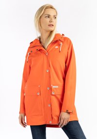 Vízálló narancssárga esőkabát kapucnival, patentgombokkal, két elülső zsebbel, állítható húzózsinórral és fehér logóval a mellkason.
