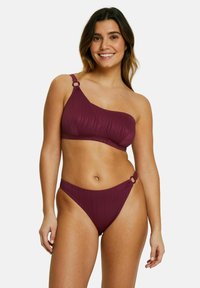 Ensemble bikini de couleur bourgogne profond, avec une texture côtelée. Haut asymétrique avec un accent en anneau ; bas taille basse assorti avec détail en anneau sur le côté.