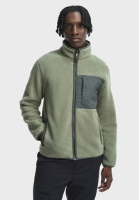 Fleece bunda v svetlozelenej farbe s textúrovaným povrchom, plným zipsom, stojacím golierom a tmavozelenou náprsním vreckom, obsahujúcim bočné vrecká.