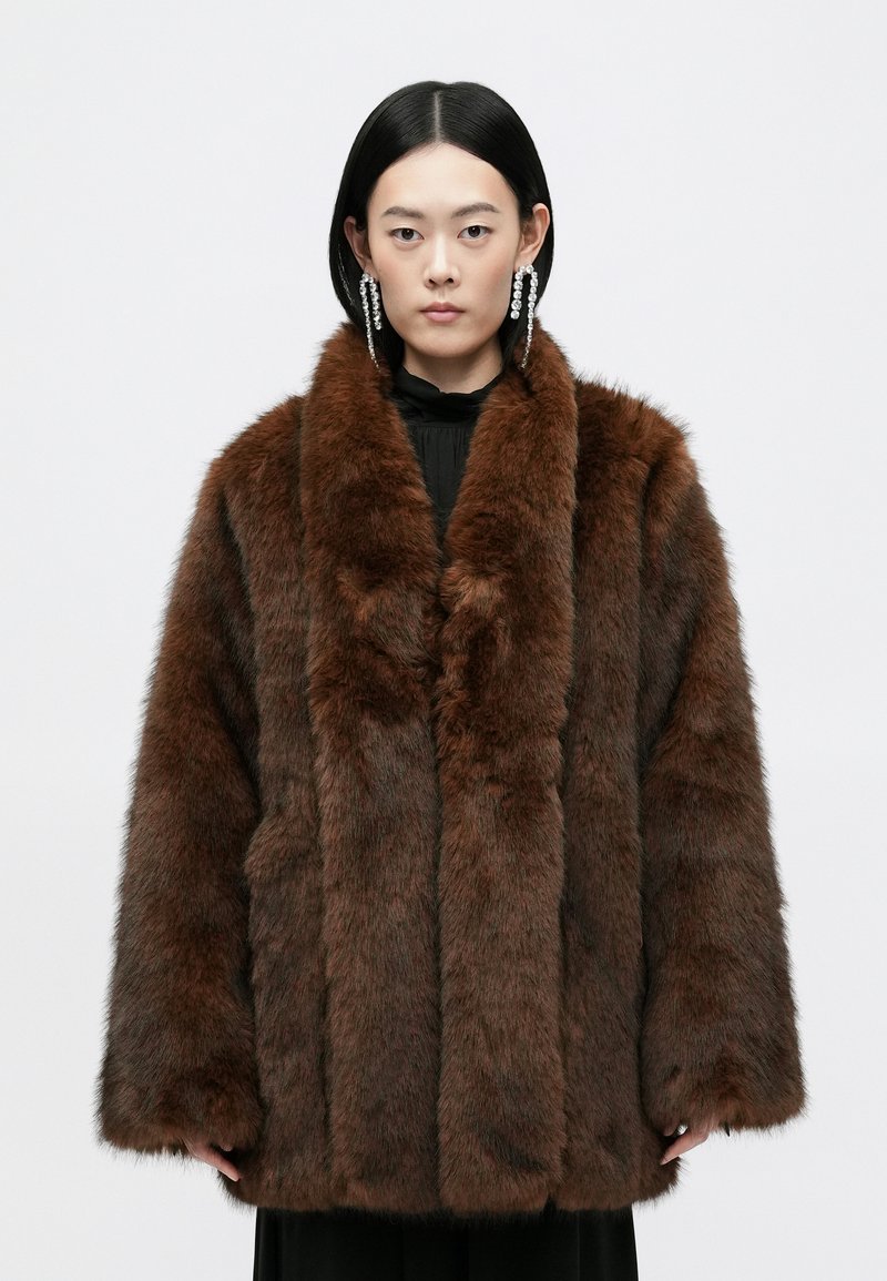 Abrigo de piel sintética marrón con un amplio cuello, mangas largas y una superficie texturizada y suave. Presenta un corte holgado y sin cierres visibles.