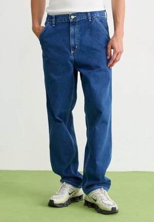 Blue denim jeans with a straight fit, featuring a front button closure, two side pockets, and slight fading on the thighs. Worn with white sneakers.