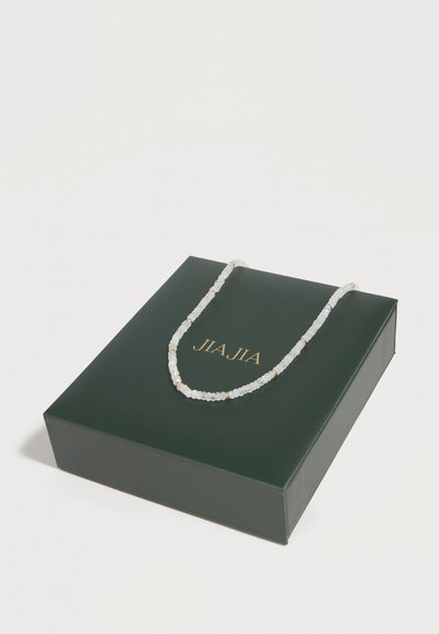 Λευκό κολιέ με χάντρες και μικρά χρυσά διαχωριστικά, τοποθετημένο σε σκούρο πράσινο κουτί με χρυσό λογότυπο "JIA JIA".