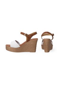 Witte wedge sandaaltjes met een gevlochten tan platform en een verstelbare bruine enkelband. Het open teen ontwerp benadrukt de gladde afwerking.