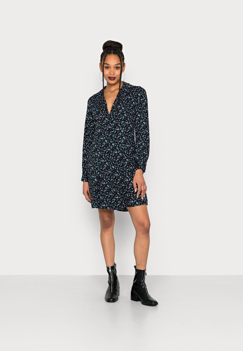 Vestido com estampado floral, com decote em V e mangas longas. Fundo preto com flores rosas e azuis. Usado com botas pretas até ao tornozelo.