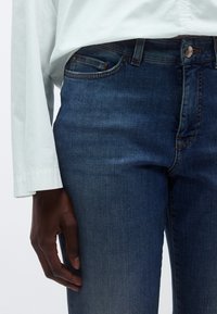 Sötétkék farmernadrág egyenes szabással, közepes derékmagassággal, finom kopott hatással és klasszikus öt zsebes kialakítással.