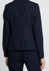 Marinblå skräddarsydd blazer med en strukturerad passform, enkel ryggslits och knappade manschetter. Slät yta med fodrade inredningsdetaljer.