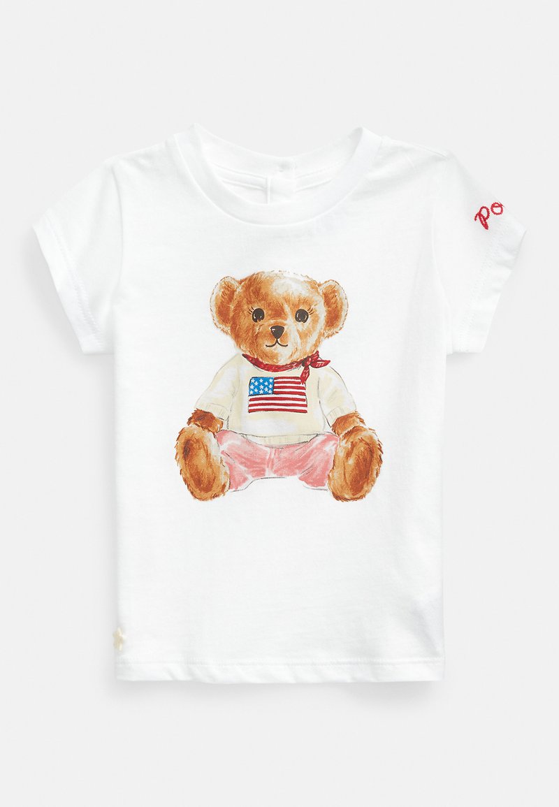 Balts kokvilnas T-krekls ar zīmējumu - teds lācis, kuram uz krekla ir ASV karogs, valkā rozā šortus un sarkanu galvas lakatu, ar īsām piedurknēm.