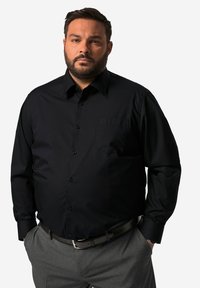 Zwarte langslievende shirt met een knopenvoorzijde, voorzien van een borstzak en een scherpe kraag, gecombineerd met grijze pantalon en een zwarte riem.