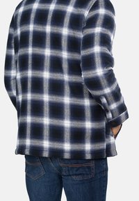 Chemise à carreaux bleu marine et blanche avec manches longues, poignets à boutons et coupe décontractée, fabriquée en tissu texturé. Portée avec un jean bleu.