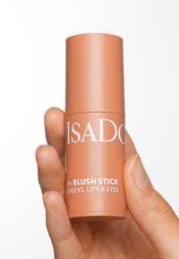 Bâton blush dans un tube cylindrique pêche. Présente un texte blanc indiquant "ISADORA" et "Le BÂTON BLUSH". Fini mat lisse et design élégant.