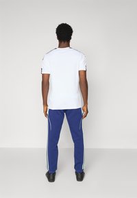 Hvit t-skjorte med korte ermer og svarte detaljer, kombinert med blå joggebukser med lyseblå sidelister. Enkelt og funksjonelt design.