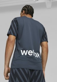 Tmavě šedý sportovní dres s černými rukávy se zigzag vzorem. Na zádech se nachází bílý text "wefox." Tkanina vypadá lehce a prodyšně.