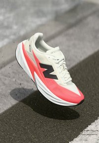 Leichter Laufschuh mit einem weißen und rosafarbenen Design, strukturiertem Obermaterial, schwarzem Logo und sportlicher Silhouette. Verfügt über eine dicke, gepolsterte Sohle.