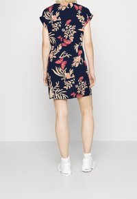 Mörkblå blommig klänning med korta ärmar, prydd med röda blommor och löviga mönster. Klänningen slutar strax ovanför knäet. Matchad med vita sneakers.