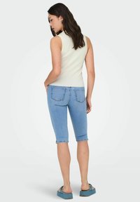 Top senza maniche color beige chiaro; bermuda aderenti blu; dettagli di cucitura sottili; modella indossa scarpe slip-on blu chiaro.