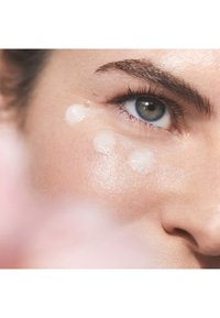 Gros plan sur un visage appliquant un produit de soin de la peau translucide et crémeux ; la peau est lisse avec une texture naturelle et une finition éclatante.