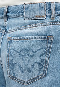 Bolsillo trasero de jeans de mezclilla azul claro con bordado de mariposa y una etiqueta de cuero cosida encima del bolsillo con la inscripción "PINKO".