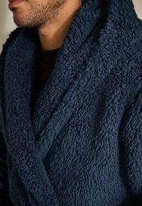 Navyblå tekstureret badekåbe lavet af blødt, fluffy stof med sjalkrave og overlappende front. Har en hyggelig, løs silhuet.