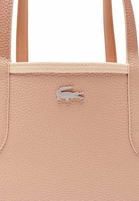Borsa tote in pelle rosa con texture che presenta un sottile logo a forma di coccodrillo sul davanti. Doppi manici con cuciture rinforzate.