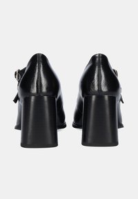 Zapatos de tacón de cuero negro con un acabado suave, punteras redondeadas y tacones gruesos. Presentan un detalle de hebilla en el lateral.