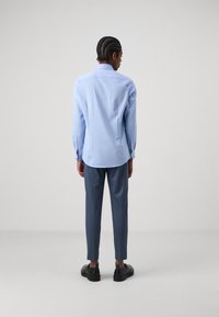 Lichtblauwe langemouwshirt met een button-down kraag, gecombineerd met grijze op maat gemaakte broek en zwarte schoenen; gladde stof en een aansluitend ontwerp.