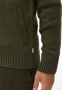 Donkergroene trui met ribgebreide manchetten en zoom, voorzien van een zijzak. Gemaakt van textuurgebreid materiaal met een label op de zoom.