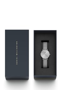 Orologio d'argento con cinturino a rete, presentato in una scatola scura con un morbido interno nero. Cifera rotonda semplice, design minimalista, finitura elegante.