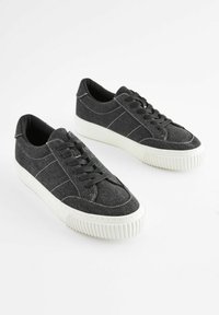 Mustad teksasesneakerid valge kummitald, millel on õmmeldud detailid ja klassikaline paeltesüs. Sile tekstuur, madal profiil.