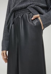 Svart läderbyxor med resårmidja, slät yta och sidofickor, parat med en något oversized grå stickad tröja.