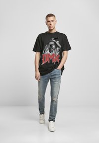 Czarna, oversize'owa koszulka z grafiką osoby z mikrofonem oraz napisem "DMX" w boldowym czerwonym kolorze. Połączona z jasnoniebieskimi przetartymi dżinsami i białymi trampkami.