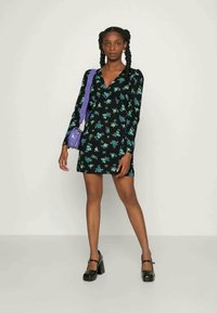 Vestuário floral preto com mangas longas, apresentando padrões azuis e verdes, combinado com uma pequena mala roxa e sapatos de plataforma pretos.