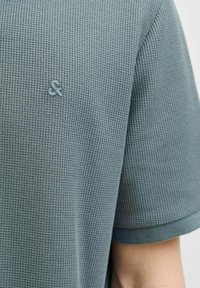 Korte mouwen T-shirt in textuurstof met een gemuteerde teal kleur, voorzien van een geborduurd ampersand-logo op de borst en contrasterende afwerking bij de mouwen.
