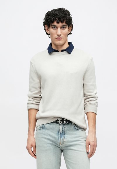 Pull gris clair avec un col bleu marine, une texture côtelée et des manches longues, associé à un jean bleu délavé et une ceinture noire avec des accessoires argentés.
