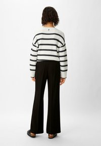 Gestreifter Pullover in Schwarz und Weiß mit lockerer Passform, kombiniert mit schwarzen weiten Hosen und schwarzen flachen Sandalen, aus strukturierter Strickware.